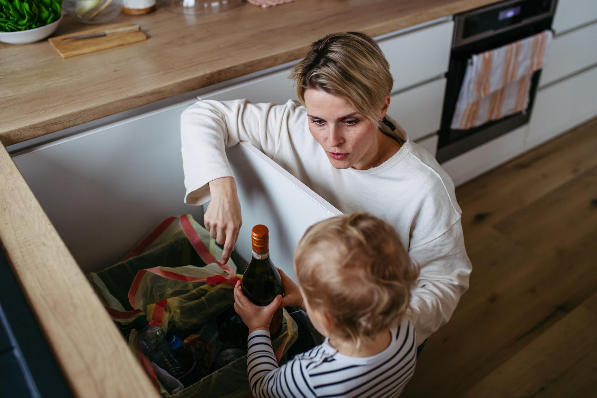 Mother teaching toddler to sort waste into recycling bin